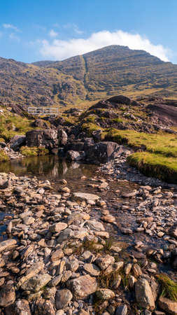 Mountain stream at the footstep of a mountain with a small white bridge.の写真素材