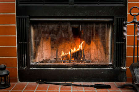 A fireplace surrounded by red bricks, with a log burning inside of it の写真素材