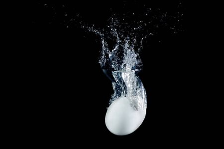 Fresh egg dropped into water with splashes isolated on black backgroundの写真素材