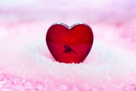 A small red heart in a pile of white and pink sugar. Sweet romantic decor