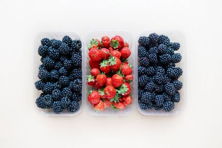 Three plastic containers full of fresh blackberries and strawberries, top view.の写真素材