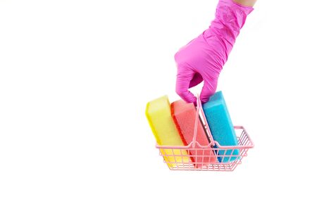 Female hand in pink nitrile gloves holds a miniature shopping basket full of multicolored dishwashing sponges. Side view, isolated on white, copy space.の写真素材