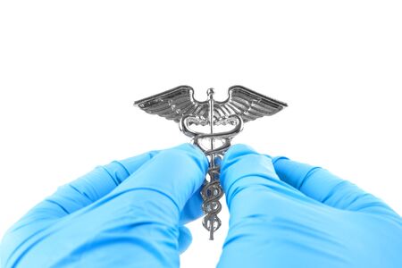 Female hands in blue disposable gloves hold a medical insignia of Caduceus isolated on white.