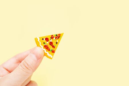 Female hand holds a tiny piece of a toy pizza on a neutral background.の写真素材