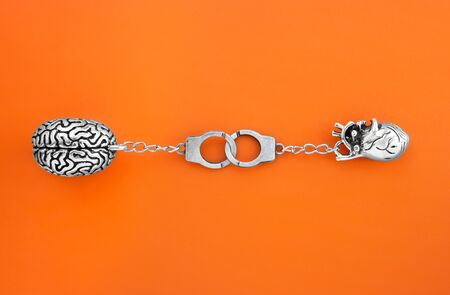 Flat lay of small steel copies of human brain and heart linked with tiny handcuffs on orange...