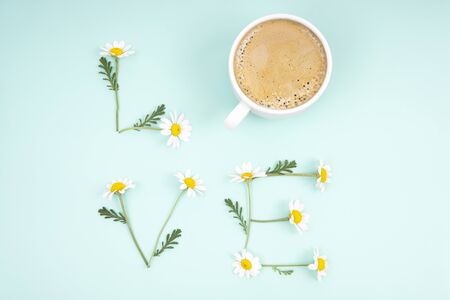 Creative romantic composition forming the word LOVE of chamomile flowers and a coffee cup on a light blue background. Vivid and tender fresh cup of love concept. Relationship refreshment idea.の写真素材