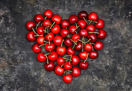 Red heart made of ripe sweet cherries on a grunge background. Romantic fruit composition.
