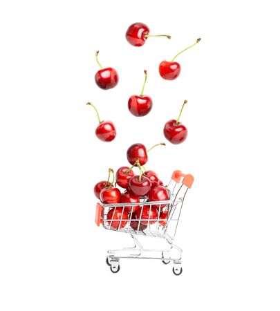 Ripe sweet cherries falling into a miniature toy shopping cart isolated on white background. Organic and weightless fruit shopping concept.の写真素材