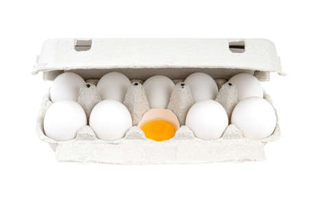 White chicken eggs in a paper carton. One half of an eggshell contains a yolk. Close-up shot, isolated on white.の写真素材