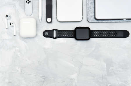 Modern everyday carry gadgets on a concrete desk: smartphone, smartwatch, digital tablet, stylus pencil, wireless earphones, memory stick. Black and white tones, copy space.の写真素材