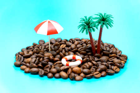 Miniature toy island made of coffee beans, palm trees, beach umbrella and lifebuoy on turquoise background imitating the ocean.の写真素材
