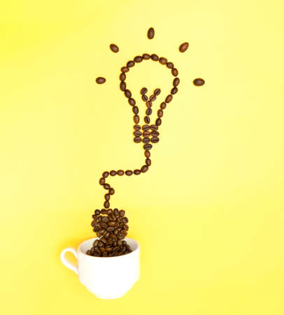Creative arrangement of roasted coffee beans resembling a glowing light bulb plugged to a white coffee cup on yellow background. Natural energy booster concept.の写真素材