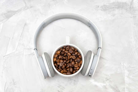 Wireless headphones on a porcelain cup full of roasted coffee beans on a concrete tableの写真素材
