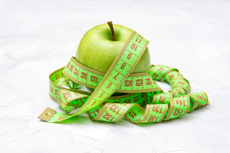 Fresh green apple with a measuring tape on a concrete table. Diet and weight loss concept.
