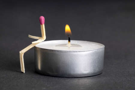 Matchstick character sitting on a lit tea candle. Loneliness and unrequited love concept.