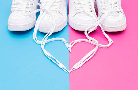 Crop view of matching white sneakers and a heart symbol made of the shoelaces on a pink blue background. Romantic concept for couples wearing matching outfits.の写真素材