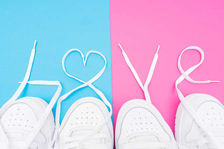 Matching white sneakers with the lettering LOVE made of the laces on a contrast blue and pink background. Matching outfits for couples idea.の写真素材