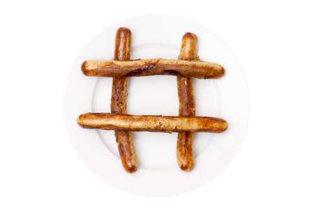Close-up of a hash symbol made of traditional grilled pork meat sausages on a large white plate isolated on a white background.の写真素材