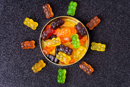 Gummy bears arranged in the shape of a sun around a candy box on a sugar coated background.の写真素材