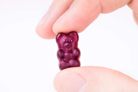 Crop view of male fingers holding a purple gummy bear against white background.