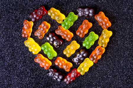 Gummy bears arranged in the shape of a heart on a sugar coated black background.の写真素材