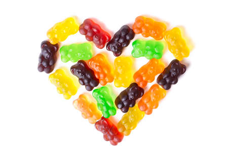 Multicolored gummy bear candies arranged in the shape of a heart on a white background.の写真素材
