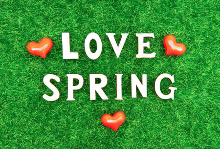 Lettering LOVE SPRING made of wooden letters and plastic hearts on green grass. Creative springtime...