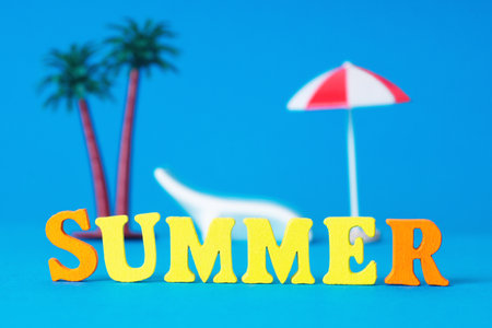 Word SUMMER made of vivid wooden letters with toy palm trees, sunbed and a parasol on the background. Creative beach vacation concept.の写真素材