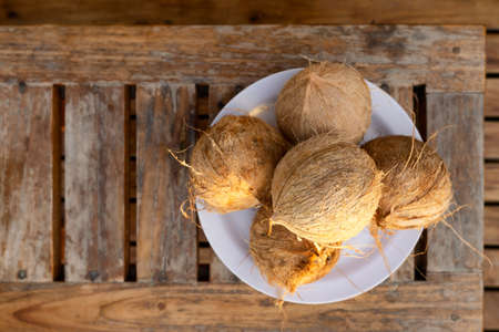 White plate with five coconuts on a wooden table, top view, selective focus.