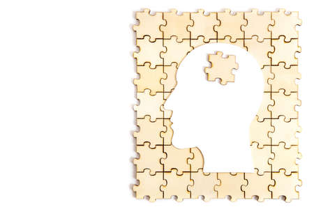 Human head shaped paper silhouette with a jigsaw piece on top of a wooden puzzle isolated on white