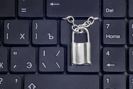 Close-up of a small locked padlock with a chain on a black laptop keyboard. Data security concept.