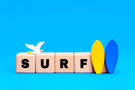 Word SURF made of wooden alphabet blocks with two surfboards figurines and a toy seagull on blue...