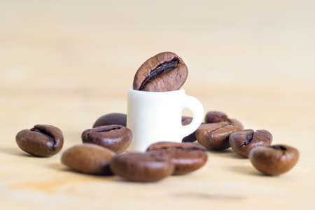 Tiny coffee cup surrounded by scattered coffee beans on a light brown background. The concept of moderate consumption.の写真素材