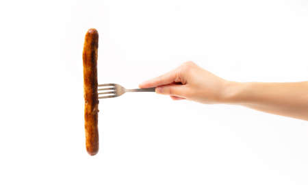 Crop view of female hand holding a fork with a grilled german sausage isolated on white background.の写真素材