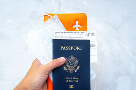 Hand holding a US passport with a vaccination record card, face mask and documents organizer in hand. International travel during covid-19.の写真素材