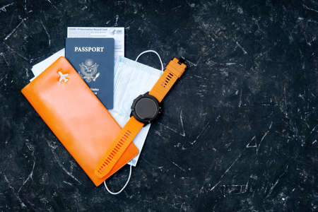 US passport with a Covid-19 vaccination record card, face mask, documents organizer and a sport smartwatch on black. Back to normal active life and travel after vaccination.の写真素材