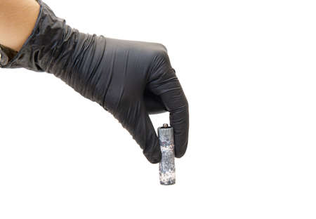 Heavily corroded AA type battery in black gloved hand isolated on white backgroundの写真素材