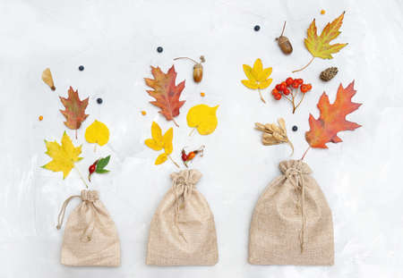 Three burlap pouches of different sizes with autumn leaves and berries on a neutral background....