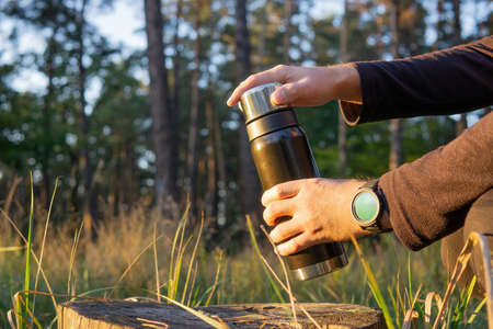 Tourist opening a vacuum thermo by a tree stump in the woods at sunset