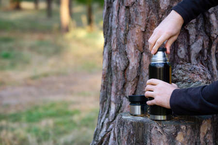 Man opening a flask bottle by a tree in the autumn forestの写真素材