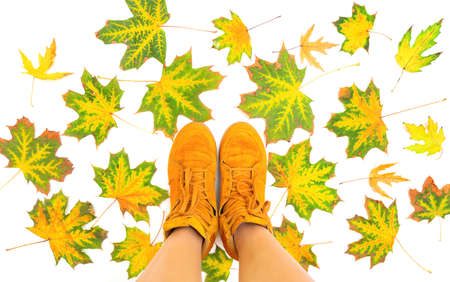Female feet in bright orange sneakers standing on pigmented leaves scattered on a white background....
