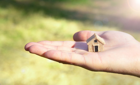 House figurine in hand against a blurred grass background. Eco-house purchase concept.の写真素材