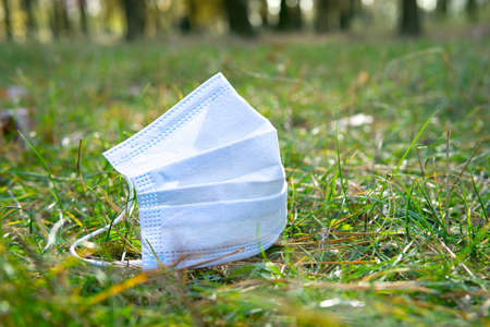 Used surgical face mask lying on the ground in the forest. Environmental pollution due to extensive use of disposable masks during pandemic.の写真素材