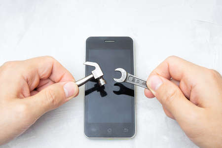 Hands holding small hand tools over a smartphone on a concrete table. Cell phone repair concept.