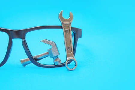 Broken sunglasses with a miniature steel hammer and wrench isolated on blue. Optics fix and repair concept.の写真素材