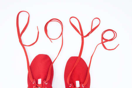 Crop view of red athletic shoes and lettering LOVE made of the shoelaces isolated on white. Love to...