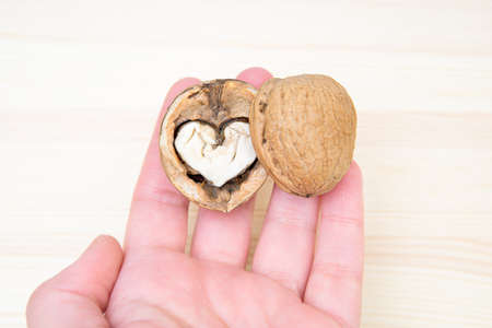 Female hand holding a heart shaped halved walnut above a wooden table