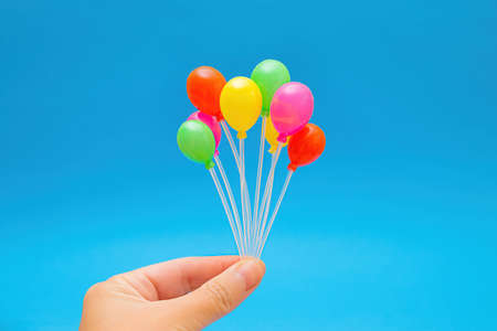 Cluster of colorful tiny plastic balloons in hand against a blue backgroundの写真素材