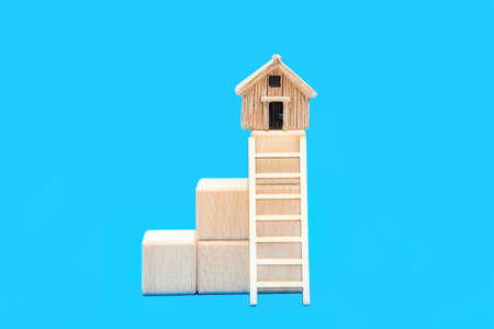 Toy ladder leading to a small house on top of stacked wooden blocks isolated on a blue background. The concept of getting on a property ladder.の写真素材