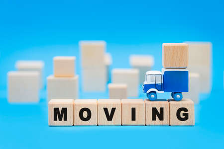 Toy truck standing on top of a line of letter blocks reading MOVING with wooden cubes in the background. Moves and relocation services concept.の写真素材